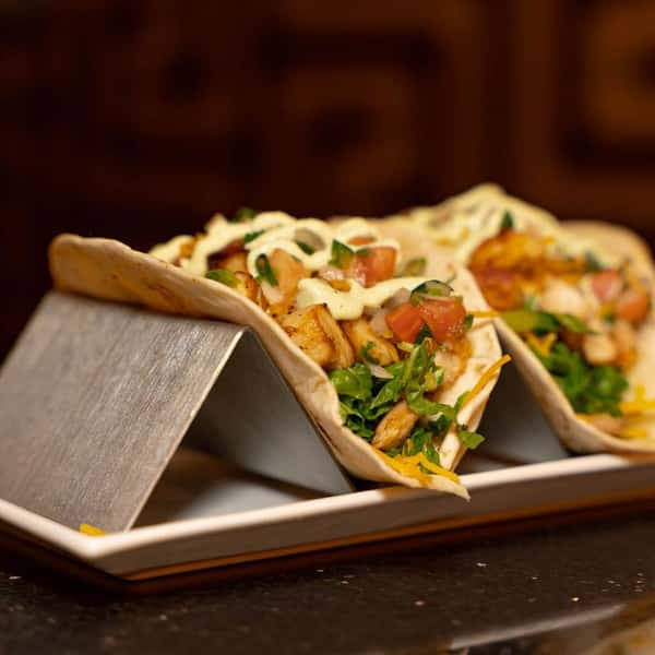 Two soft shell tacos filled with grilled chicken, diced tomatoes, shredded lettuce, and a drizzle of creamy sauce.