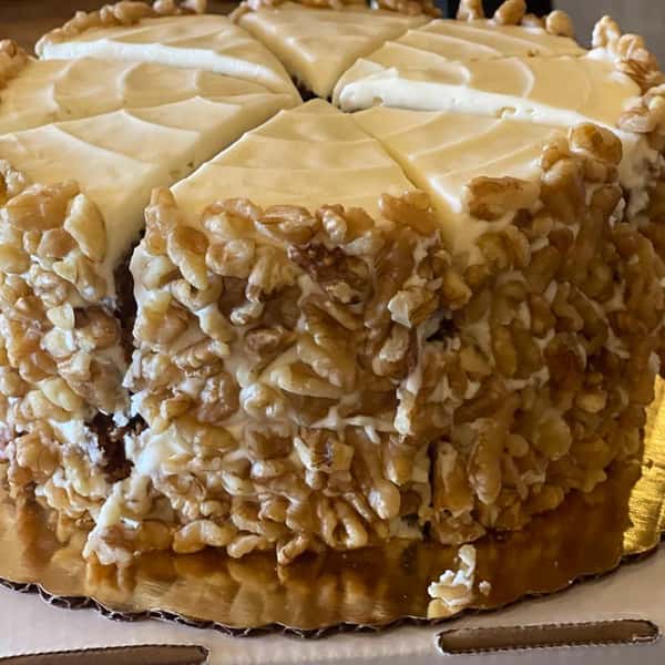 Carrot cake topped with cream cheese frosting and coated on the sides with chopped walnuts, sliced and ready to serve.