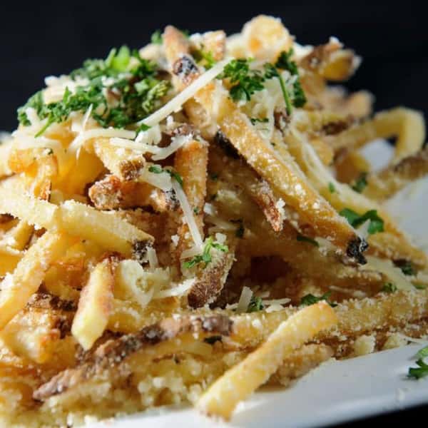 A generous serving of truffle fries topped with grated parmesan cheese and chopped parsley, served on a white plate.