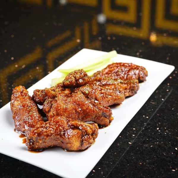 Crispy chicken wings coated in a glossy, spicy sauce served with celery sticks on a white rectangular plate.