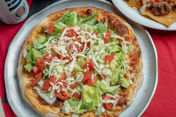 Taco pizza topped with beef, tomatoes, cheese, and lettuce