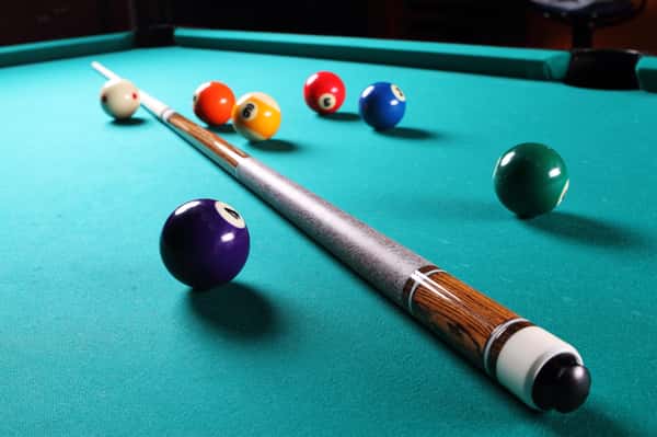 Billiard stick laying on billiard table surrounded by scattered balls