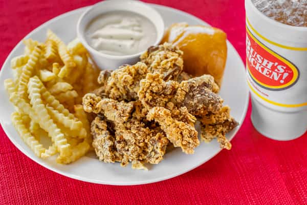Fried chicken livers meal served with crinkle-cut fries, a warm dinner roll, creamy white gravy, and an iced drink on a white plate over a red tablecloth.