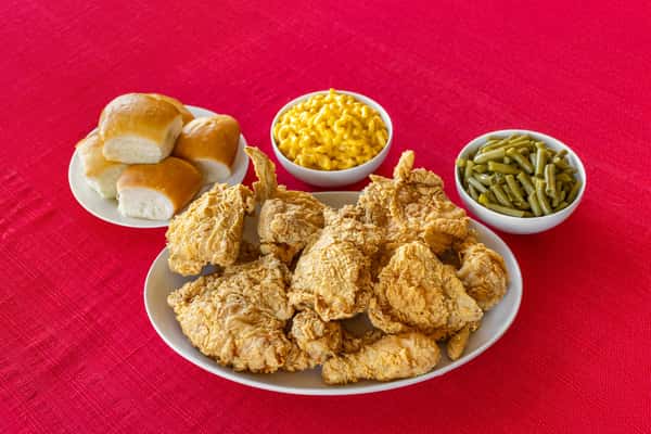 Southern fried chicken platter accompanied by buttery dinner rolls, mac and cheese, and green beans, all served on a red cloth for a comforting family meal presentation.