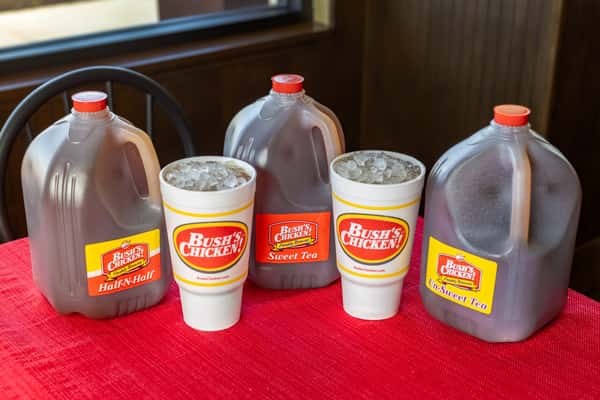 Bush's Chicken tea variety display with large jugs of Half-N-Half, Sweet Tea, and Unsweet Tea, alongside branded iced drink cups on a red tablecloth.