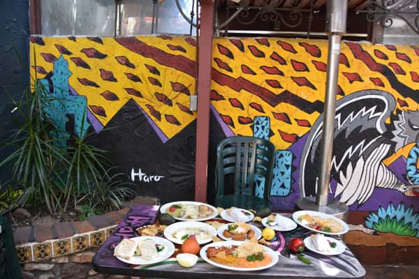A vibrant outdoor dining setup at La Cabaña with plates of delicious Mexican food, accompanied by colorful murals on the wall.