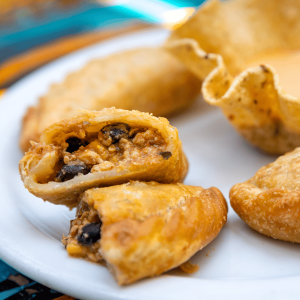 Golden empanadas filled with seasoned meat, beans, and vegetables, served on a white plate.