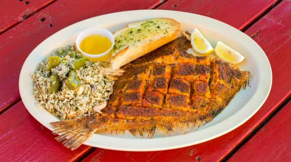 Fried fish with rice, green peppers, garlic bread, lemon wedges, and a bottle of Corona Extra beer.