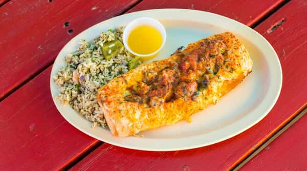 Baked fish topped with melted cheese and crayfish, served with rice and a cup of butter, on a red wooden table.