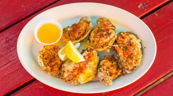 Baked oysters with cheese, herbs, lemon wedges, and a side of butter on a white plate.