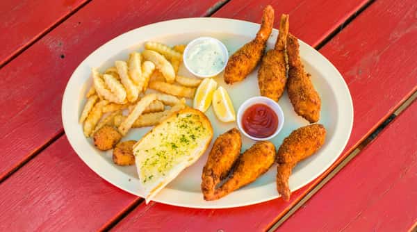 Fried shrimp basket with french fries, lemon wedges, garlic bread, tartar sauce, and ketchup on a white platter.