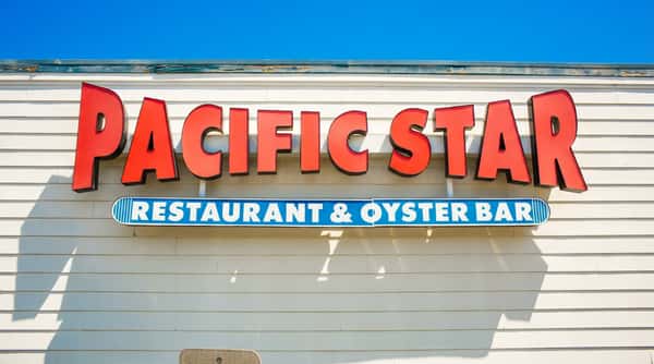 Red "PACIFIC STAR" sign with a blue "RESTAURANT & OYSTER BAR" sign on a white slatted building.