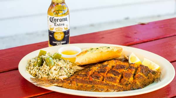 Fried whole flounder with rice, bell peppers, garlic bread, lemon, and butter on a white plate.