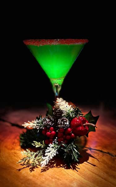 Green Martini glowing under light w holiday greenery + berries at base