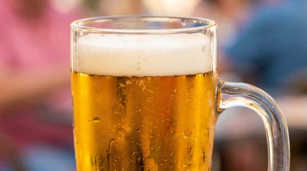 Close-up of a glass mug filled with golden beer, topped with white foam and condensation on the glass.
