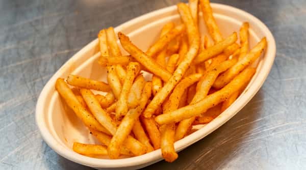 French fries seasoned with pepper, served in an oval light beige container on a metallic surface.
