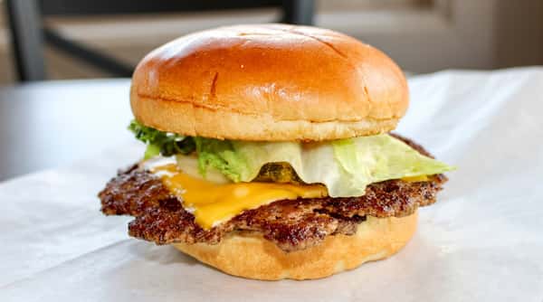 Bacon cheeseburger with crisp lettuce, white onion, and a dark patty on a golden bun, served on a textured plate.