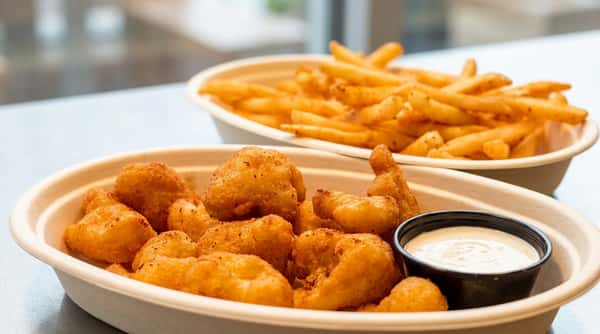 Fried cheese curds with a side of white dipping sauce, and a blurred bowl of seasoned french fries in the background.