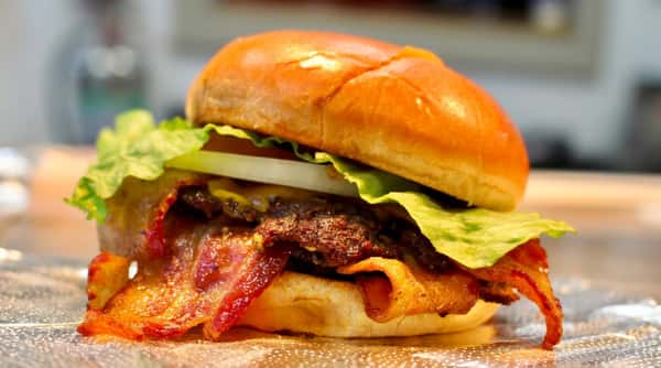 Bacon cheeseburger with crisp lettuce, white onion, and a dark patty on a golden bun, served on a textured plate.