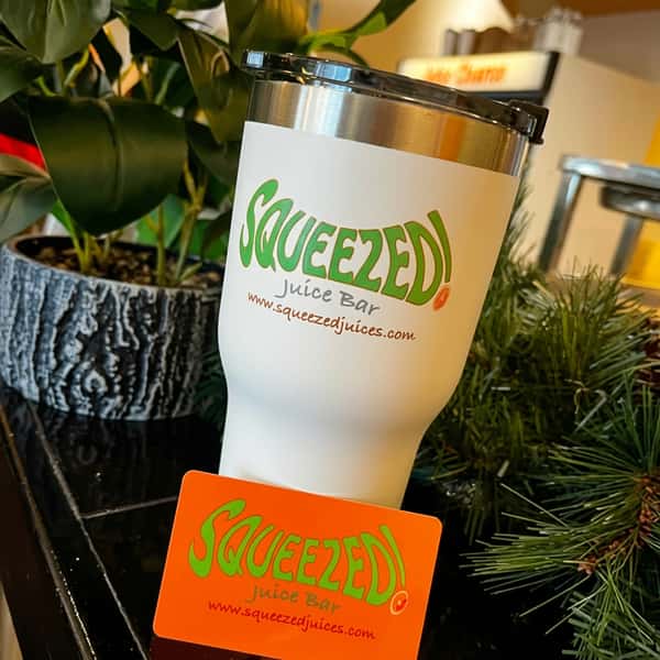 Squeezed Juice Bar branded reusable tumbler with straw next to a gift card, styled with greenery for a clean, lifestyle-focused presentation