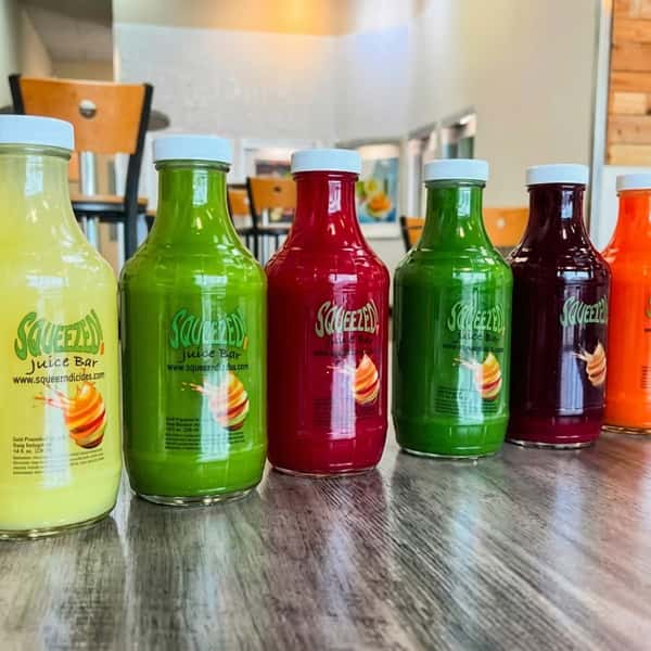 A shelf of bottled juices: bright orange, green, and pale yellow, each labeled "Squeezed."