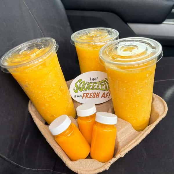 Three large and three small cups of yellow liquid on a brown cardboard tray, with a round white sticker.