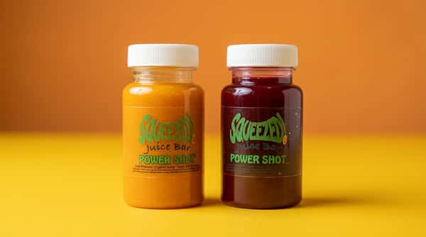 Cold-pressed wellness juice shots in small bottles, orange and deep berry blends on a bold yellow background