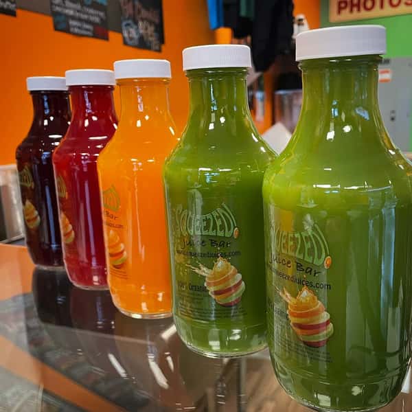 A shelf of bottled juices: bright orange, green, and pale yellow, each labeled "Squeezed."