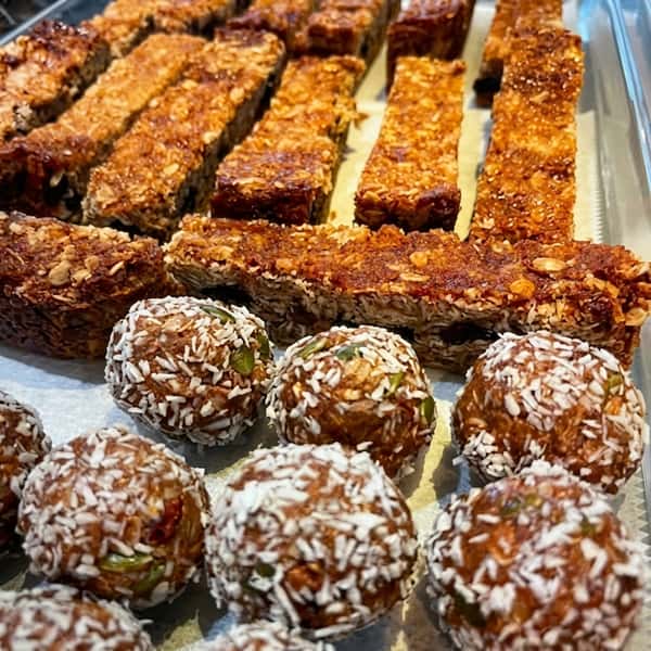 Freshly made energy bites coated in coconut and house-made granola bars displayed in a bakery tray at a healthy juice bar