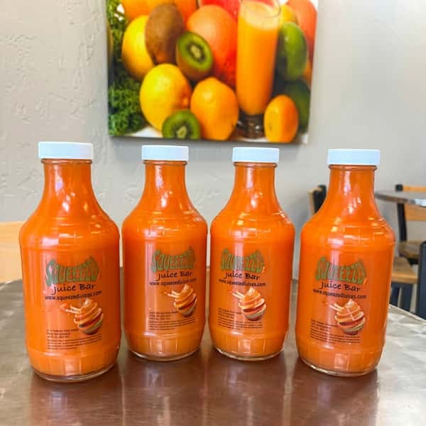 Bottles of cold-pressed juice from Squeezed Juice Bar on a shelf, in colors from orange to green.
