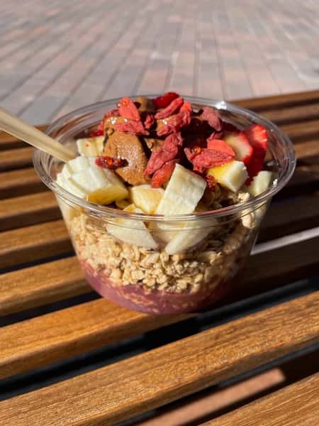 Acai bowl with granola, sliced bananas, and strawberries in a clear plastic cup.