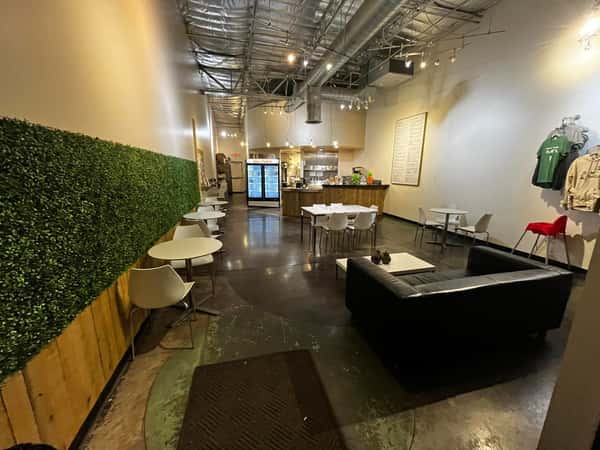 Modern juice bar interior with communal wooden tables, greenery wall, and industrial lighting creating a clean, welcoming café atmosphere