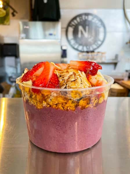 Acai smoothie bowl topped with strawberries, granola, coconut, and banana slices on a juice bar counter