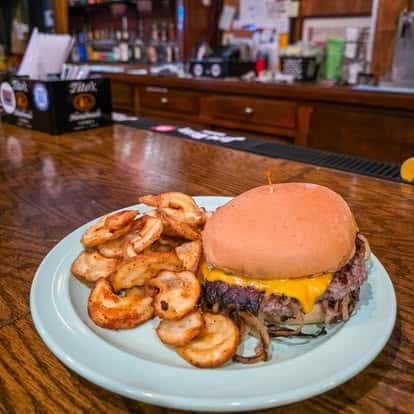 Cheeseburger with melted cheddar and grilled onions served with crispy potato rounds on a plate at a cozy restaurant bar