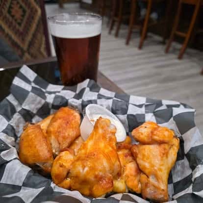 Basket of buffalo chicken wings with creamy dipping sauce served alongside a pint of amber beer