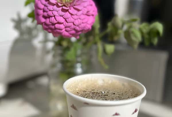 A close-up of a paper coffee cup sitting next to a vase holding a bright pink zinnia flower.