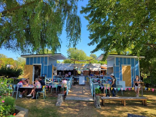 A wider shot showing small blue wooden huts and picnic tables set up under trees in a park.