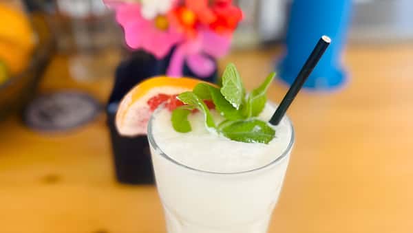 A glass filled with a white frozen slushy drink, garnished with fresh mint and a slice of pink grapefruit.