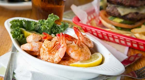 Seasoned steamed shrimp with lemon wedges and green lettuce in a white bowl.
