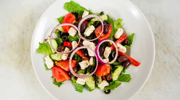 Greek salad with lettuce, tomatoes, cucumbers, black olives, red onion rings, and feta cheese.