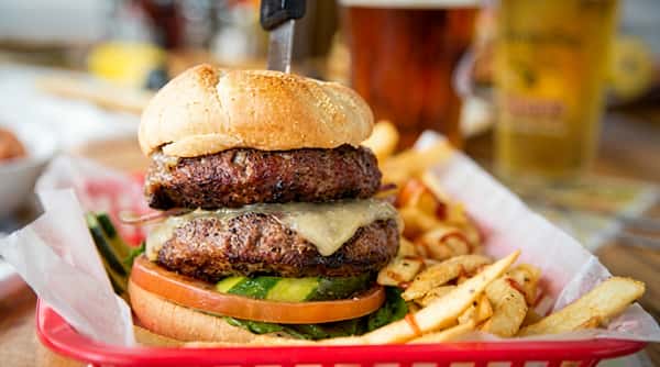 Double cheeseburger with lettuce, tomato, and pickles, served with fries in a red basket.