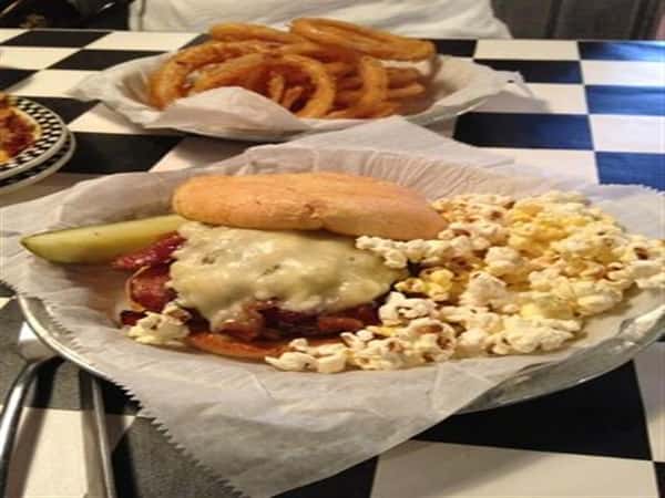 Bacon cheese burger with a side of popcorn and a pickle slice