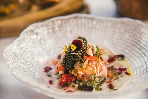 A gourmet seafood ceviche beautifully presented in a textured glass bowl, topped with caviar and edible flowers.