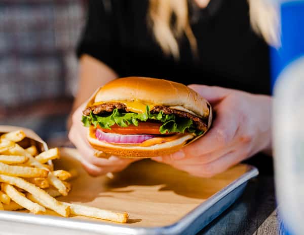 Hand holding a burger with fries