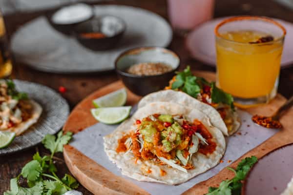 Mexican tacos topped with fresh guacamole, pico de gallo and lime, served on a wooden board with a drink