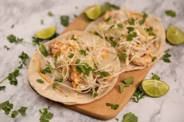 Shrimp tacos garnished with fresh cilantro and served with lime wedges on a wooden board