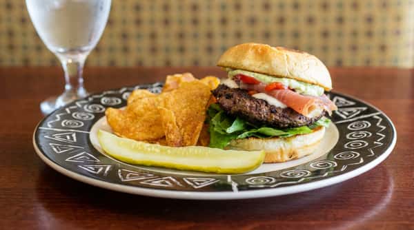Gourmet restaurant burger with lettuce, prosciutto, roasted peppers, and creamy sauce, served with house chips and pickle at Tanino Ristorante Italiano.