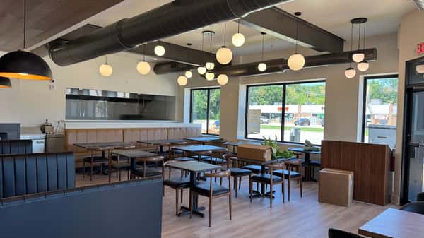 Restaurant dining room with black tables and chairs, pendant lighting, and exposed ceiling beams