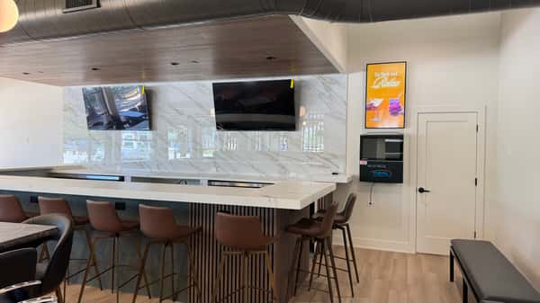 Restaurant bar area with white marble countertop, wooden stools, and a wall-mounted TV
