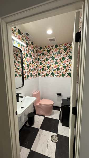 Restroom with floral wallpaper and pink accent stool